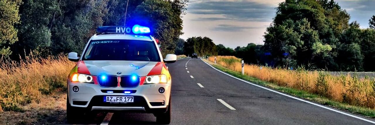 Ein Einsatzfahrzeug des DRK-Ortsverein Altrhein e.V. auf einer Landstraße mit Blaulicht stehend